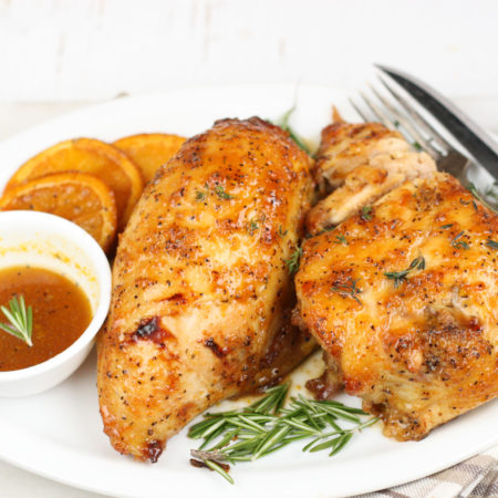 orange honey glazed chicken on a white plate with dipping sauce