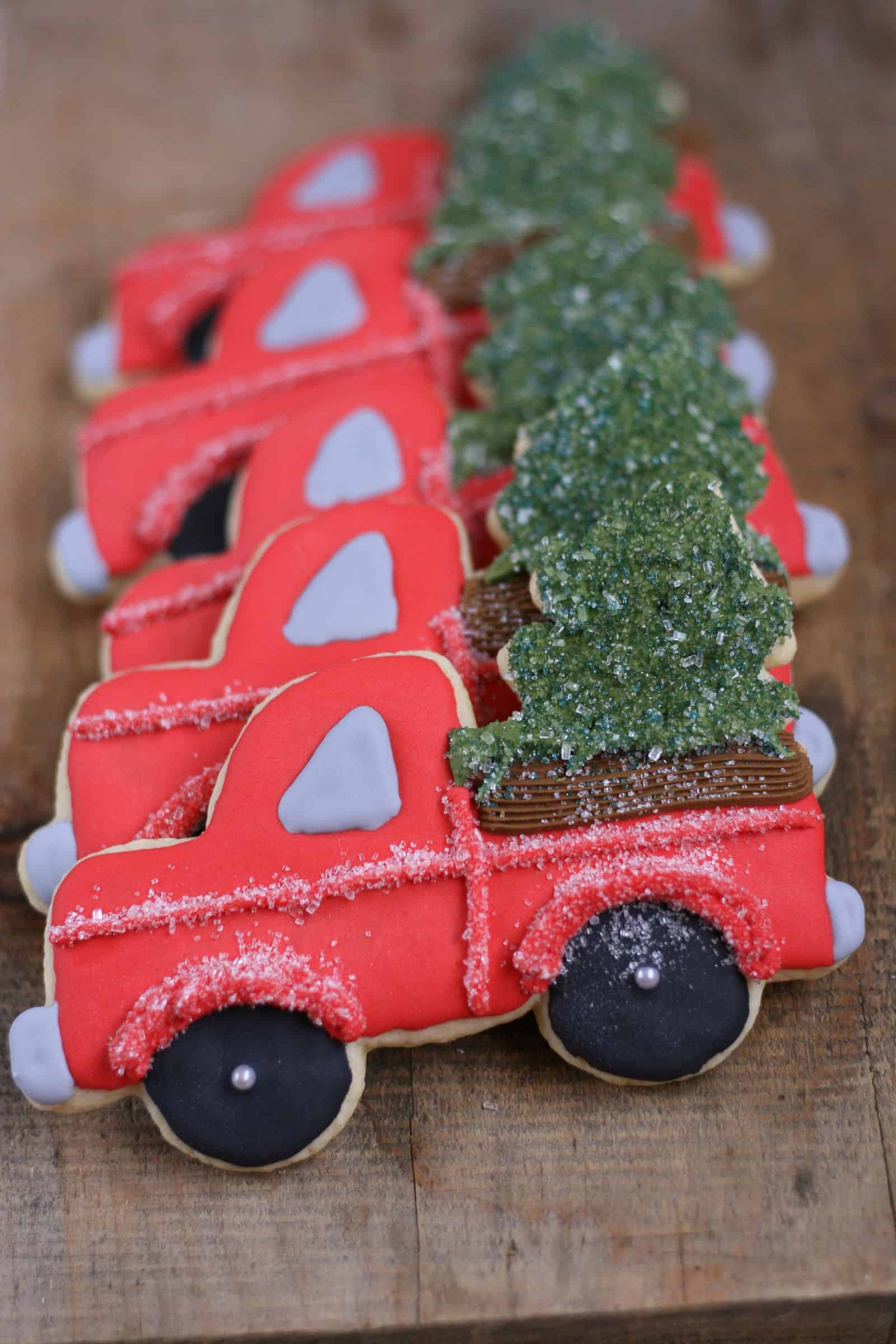 Decorated Sugar cookies vintage red trucks with Christmas tree in the back of the truck bed.