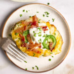 Twice baked potato on small white speckled plate with fork.