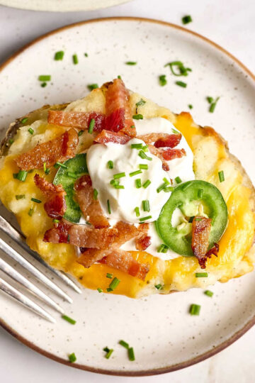 Twice baked potato on small white speckled plate with fork.