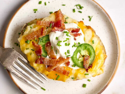 Twice baked potato on small white speckled plate with fork.