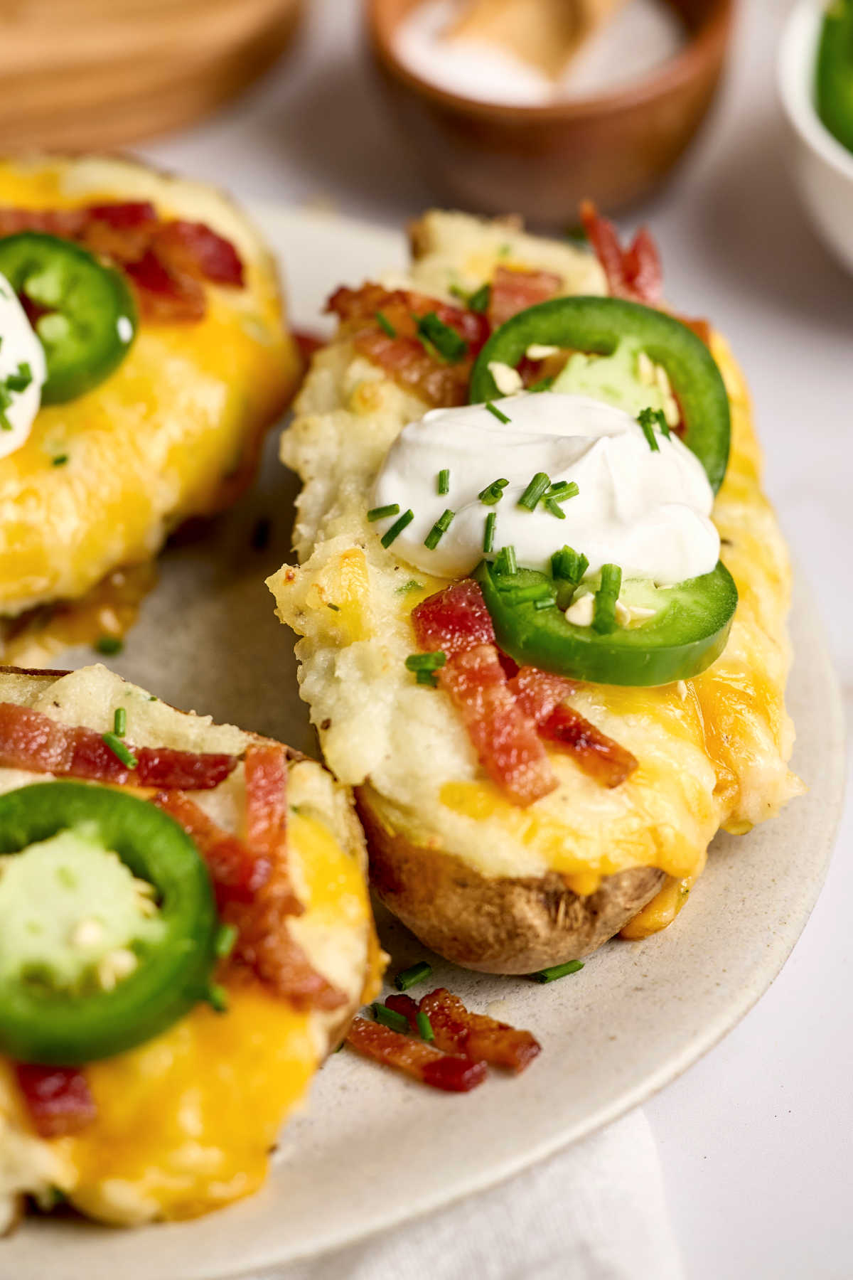 Twice baked potatoes on small plate, topped with sour cream, bacon pieces, jalapeno slices.