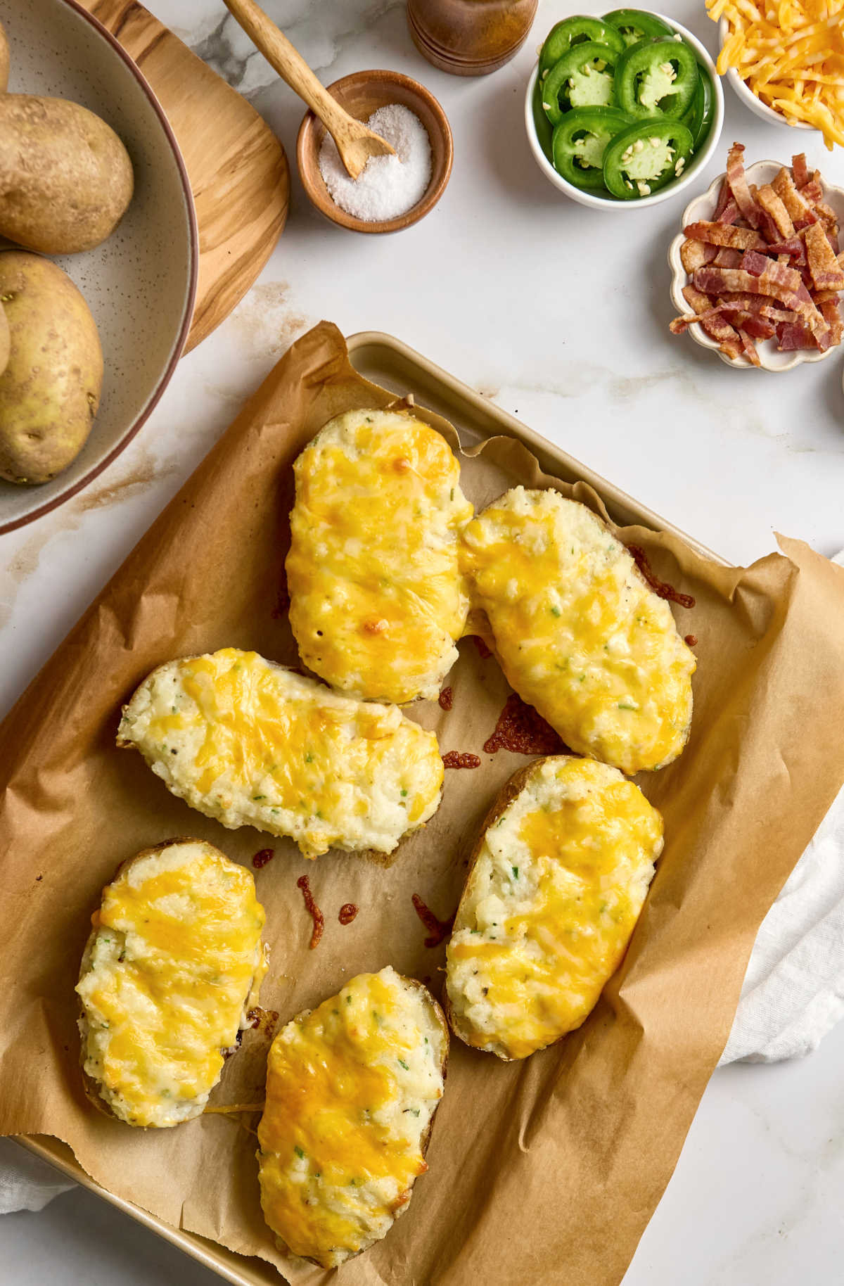 Twice baked potatoes with cheese on sheet pan, toppings in small bowls to side.