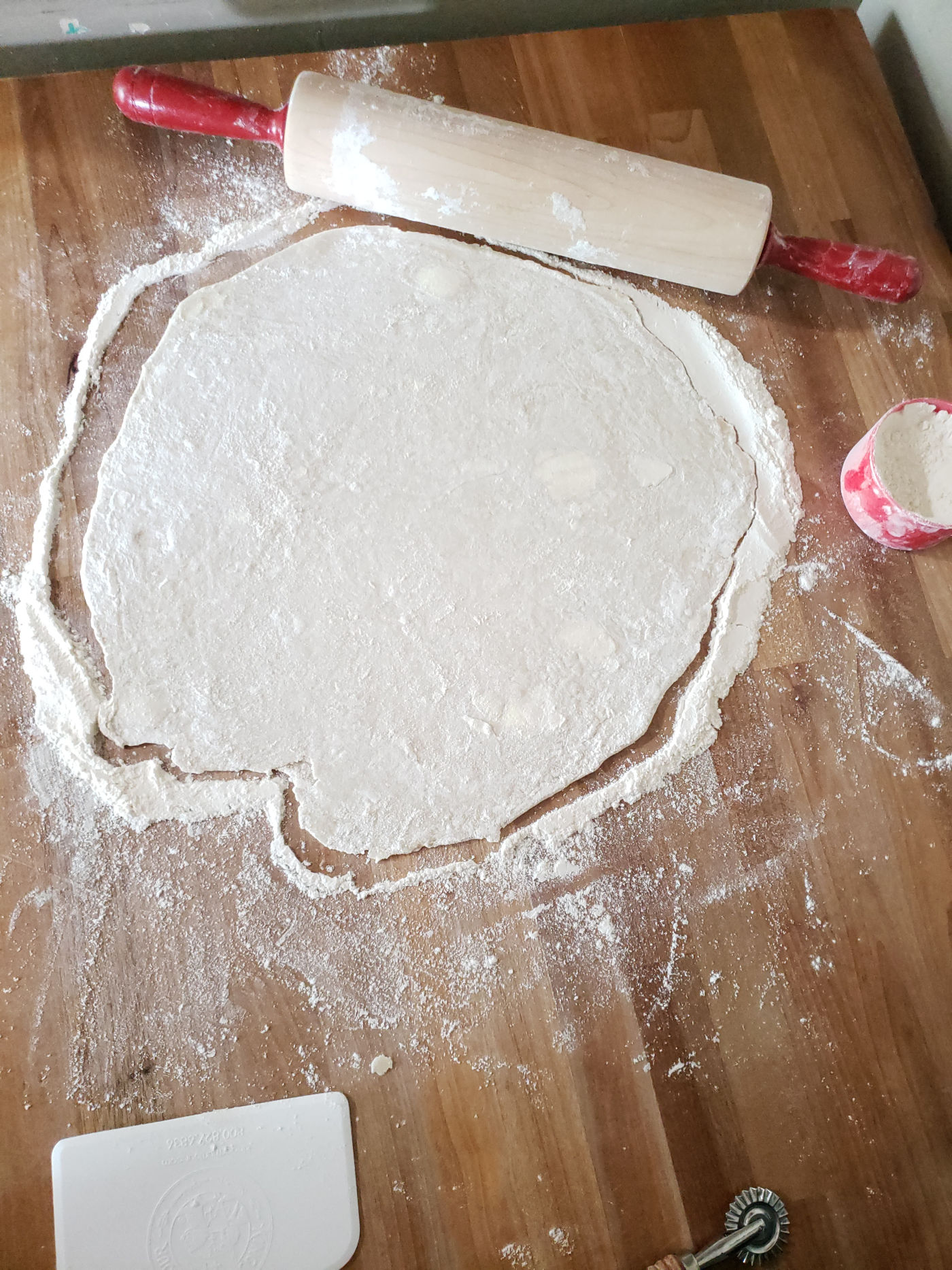 pie crust circle on butcher block. red handle wooden rolling pin behind.