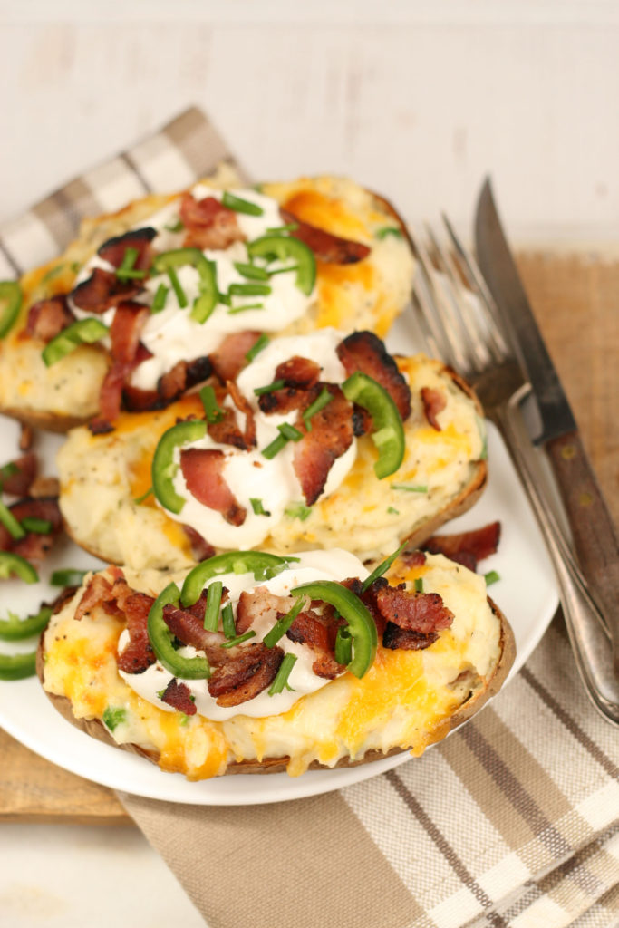 loaded twice baked potatoes on a dish with fork and knife