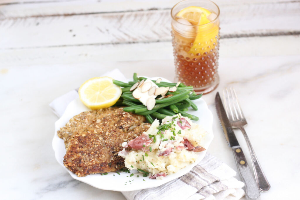 Almond crusted Tilapia filets with fresh green beans and smashed red potatoes on a white plate