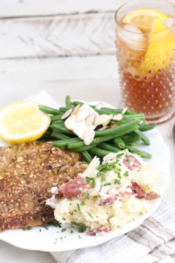 Almond crusted Tilapia filets with fresh green beans and smashed red potatoes on a white plate