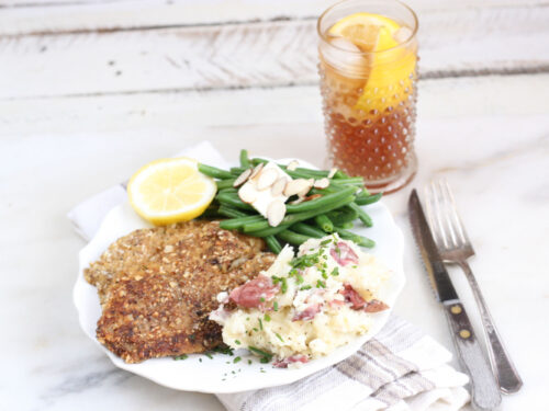 Almond crusted Tilapia filets with fresh green beans and smashed red potatoes on a white plate