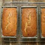 Three loaves of banana bread in metal baking pans cooling.