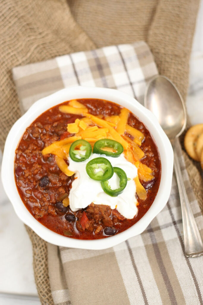 chili with beans in a bowl, topped with sour cream, cheddar cheese, and jalapeno slices