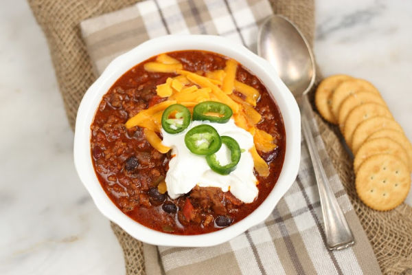 beef chili in a bowl, topped with sour cream, cheddar cheese, and jalapeno slices.
