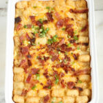 tater tots and bacon on top of a breakfast casserole in white casserole dish