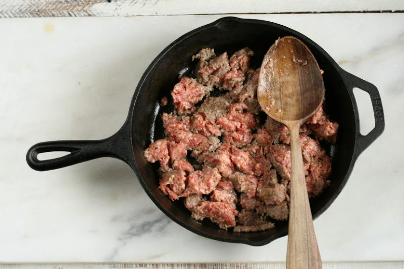 cast iron skillet browning breakfast sausage with a wooden spoon