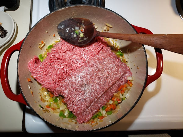 browning ground beef and pork in a red Dutch oven with wooden spoon