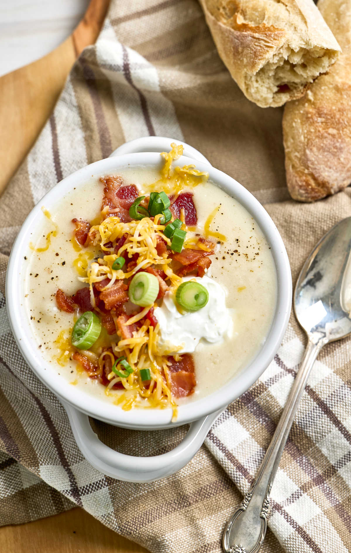 Potato soup in white soup crock, bread in background.