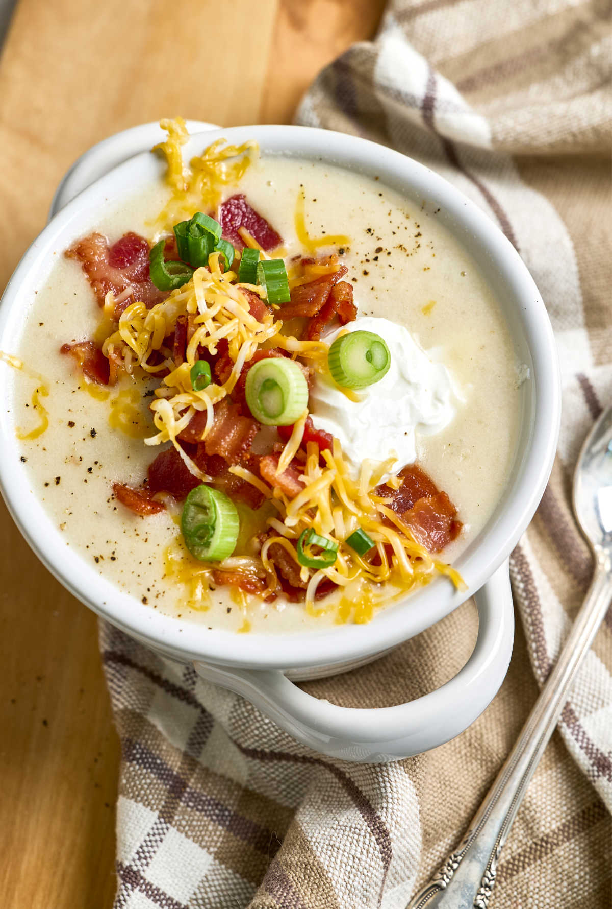 Soup in white soup crock topped with bacon pieces, cheese, green onion slices and sour cream.