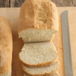 Loaf of sourdough bread partially sliced on wooden cutting board.