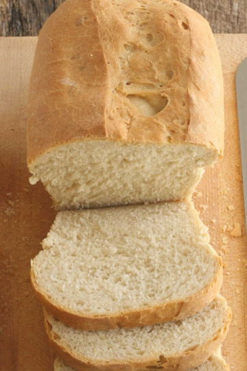 Loaf of sourdough bread partially sliced on wooden cutting board.