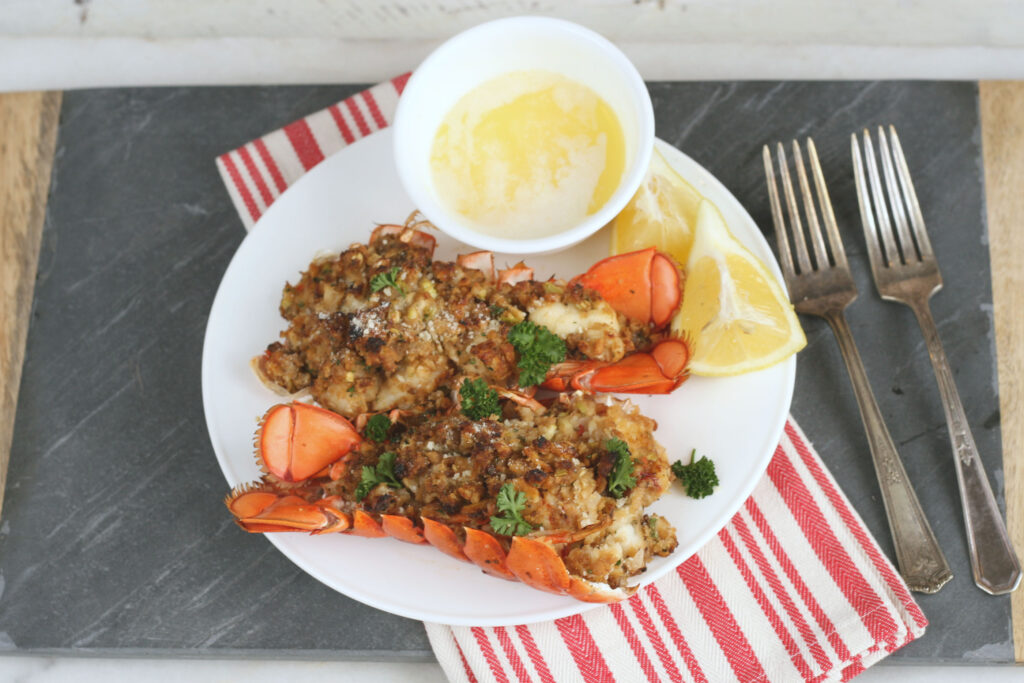 baked stuffed lobster tails on a white plate with melted butter