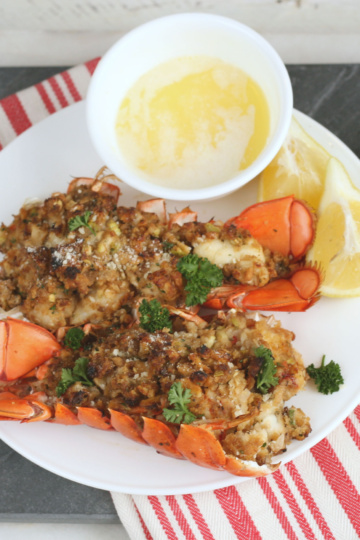 baked stuffed lobster tails on a white plate with melted butter