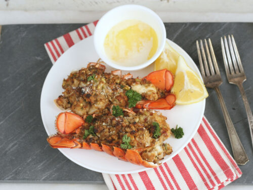 baked stuffed lobster tails on a white plate with melted butter