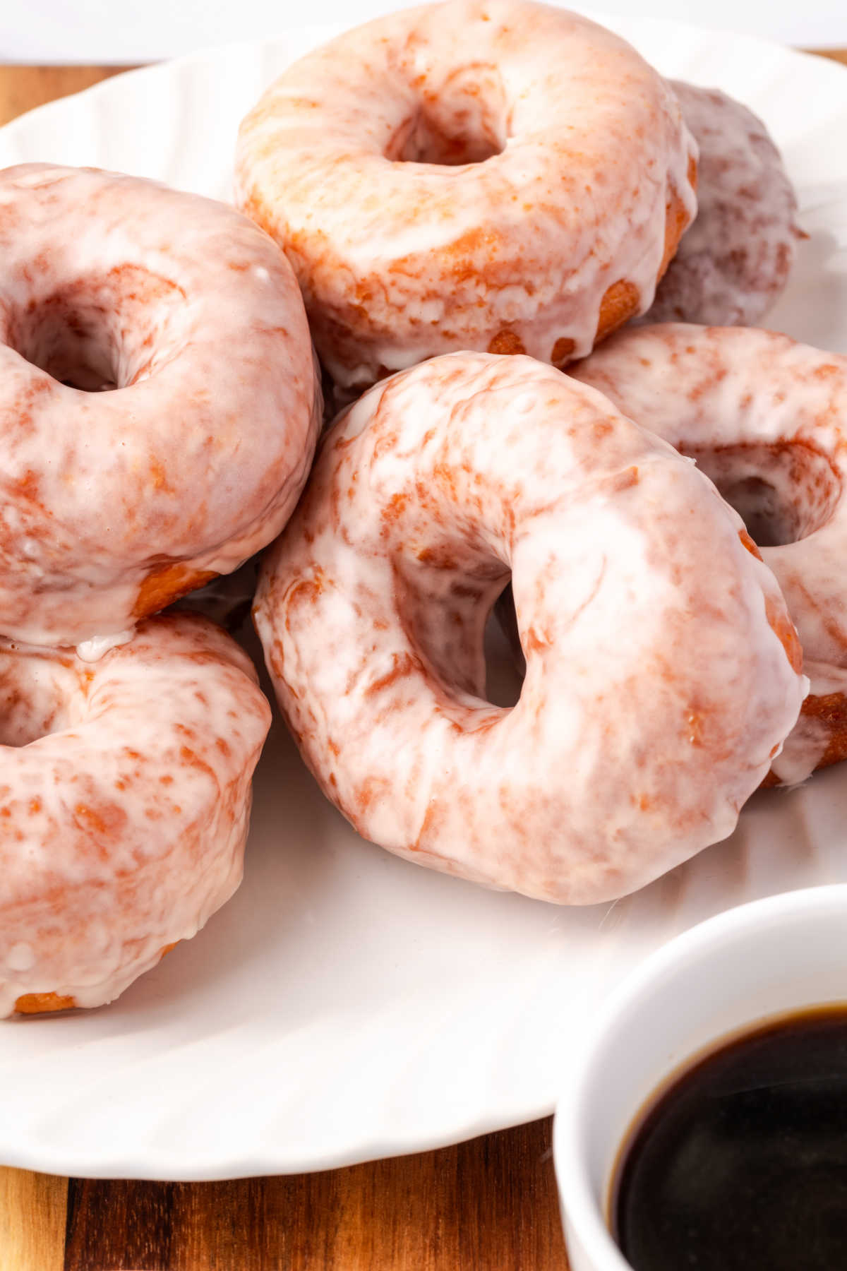 Glazed donuts piled on white plate.