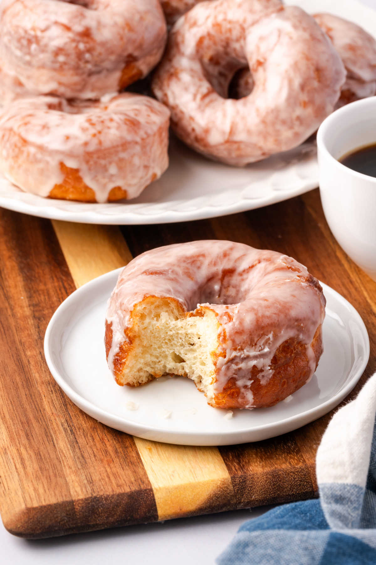Glazed donut with bite on small white plate.