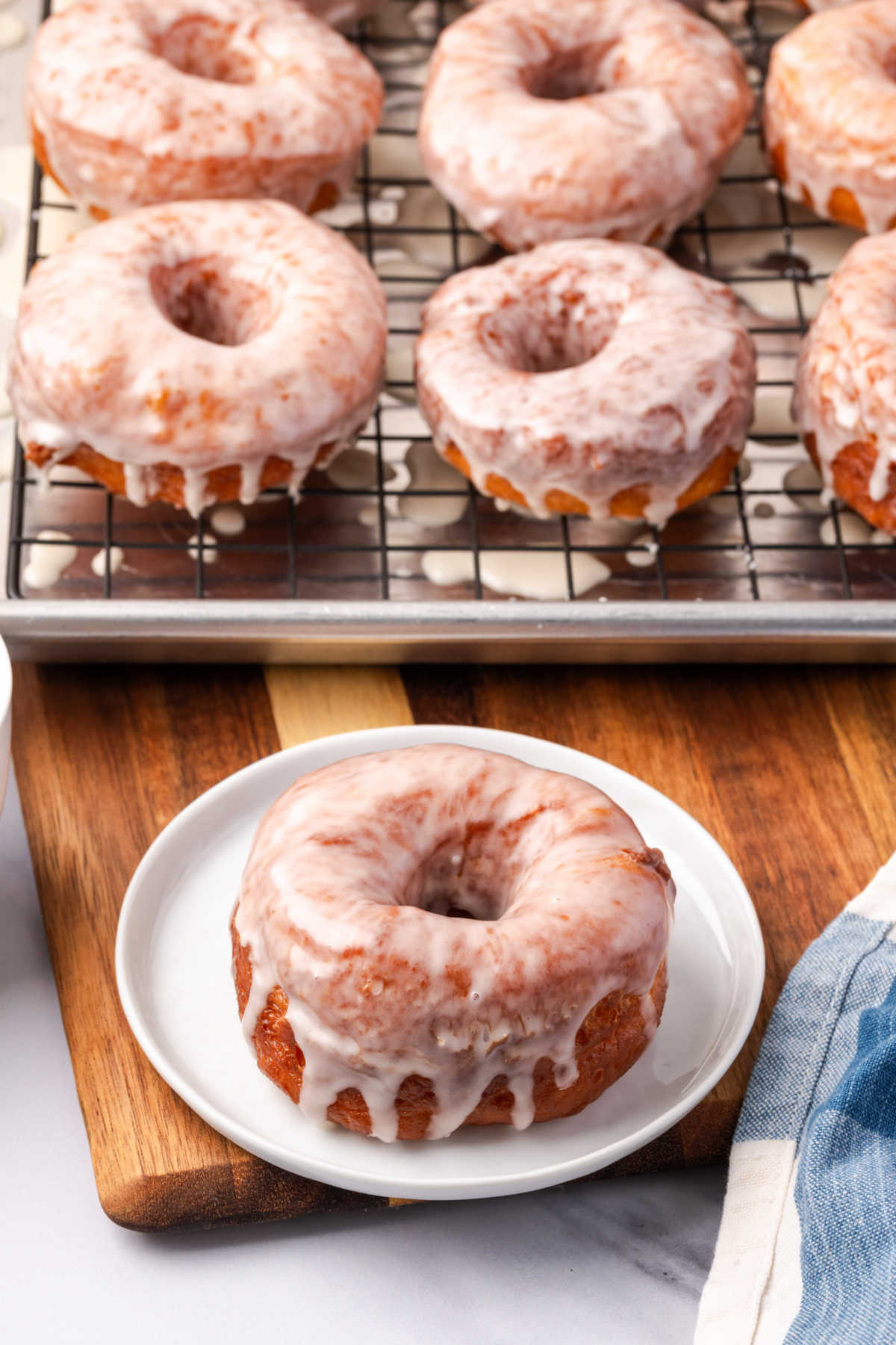 Donut on small glass plate, donuts in background on baking rack.