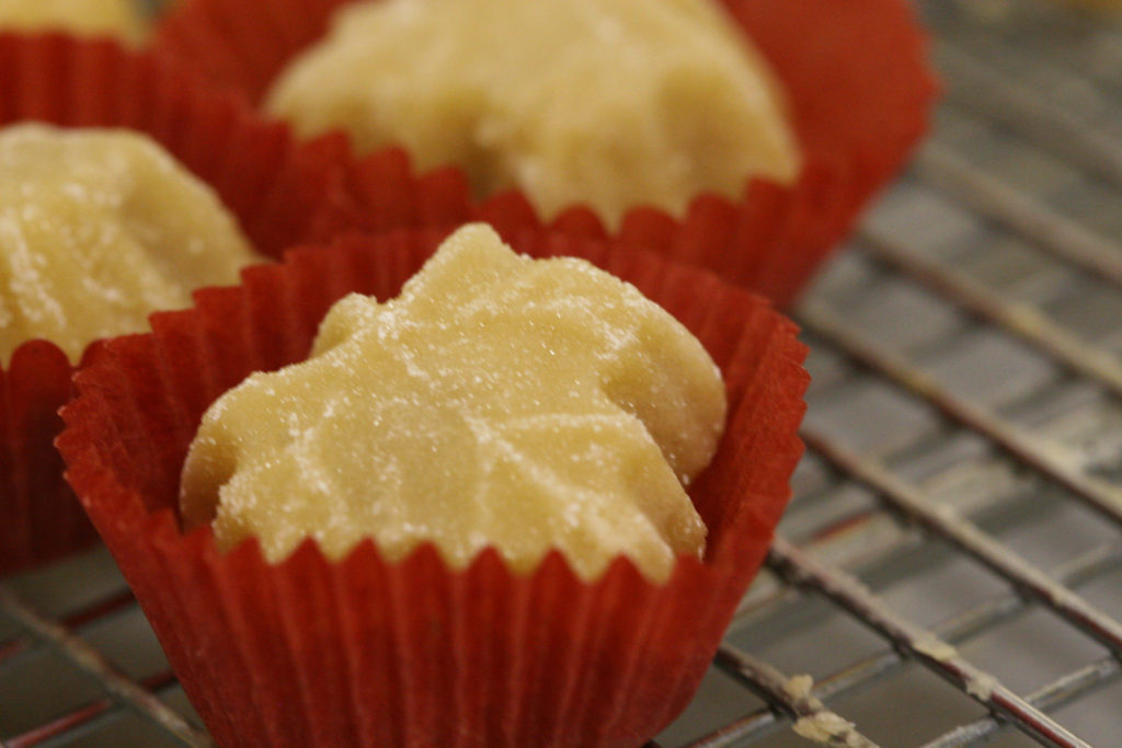 maple leaf shaped pure maple candies in deep red candy papers sitting on a baking rack