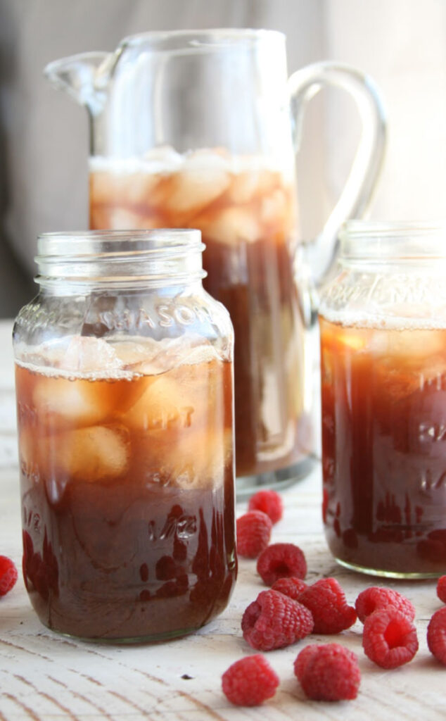 glass pouring pitcher with iced tea, Mason jars with ice and iced tea, loose raspberries surrounding