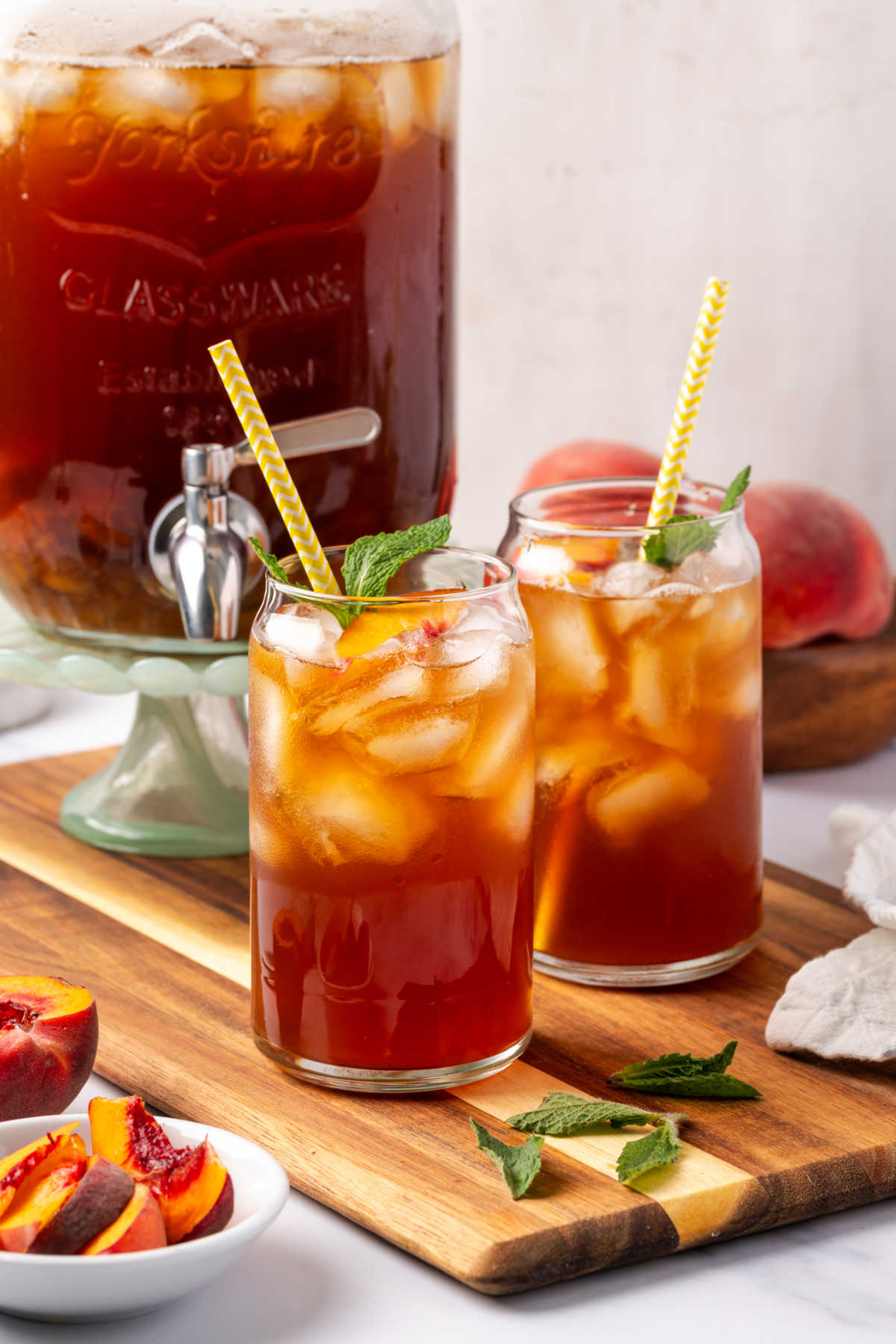 Iced tea in glasses with peach slices, fresh mint, yellow paper straws.