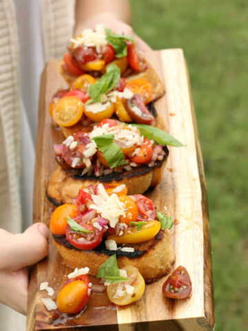tomato bruschetta with heirloom cherry tomatoes, fresh basil, shaved Parmesan cheese, on wooden cutting board