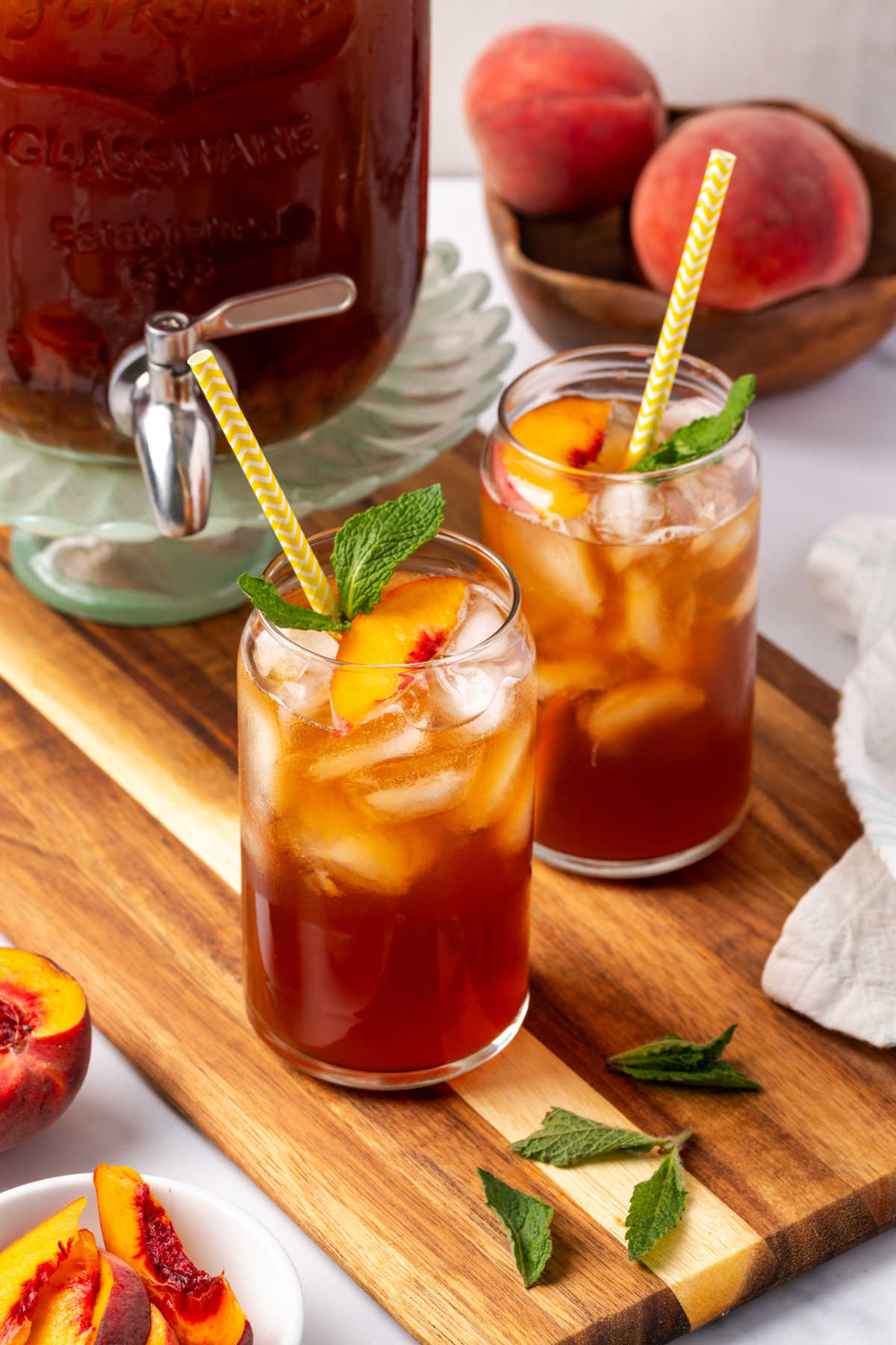 Glasses of iced tea, peach slices, fresh mint, yellow paper straws.