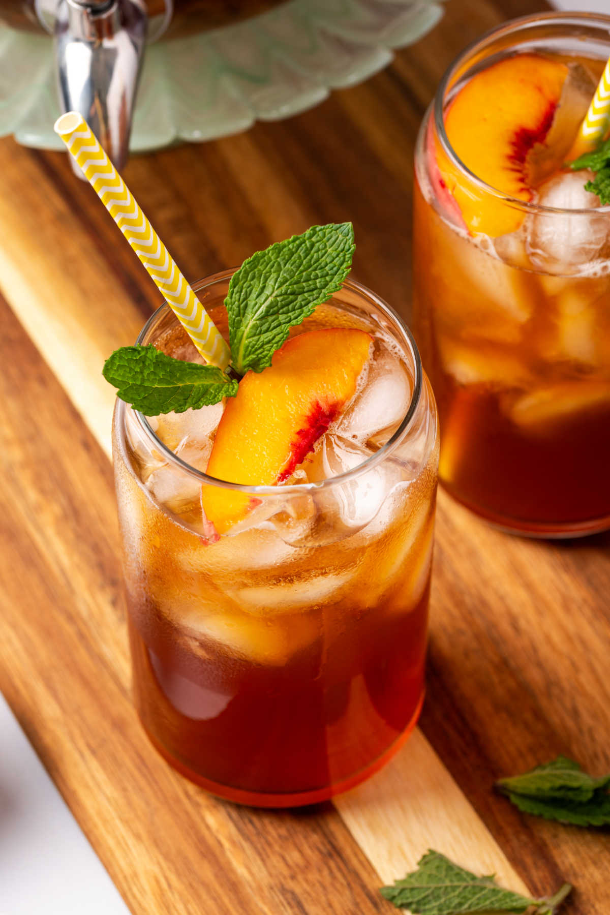 Glasses of iced tea, peach slices, fresh mint, yellow paper straws.