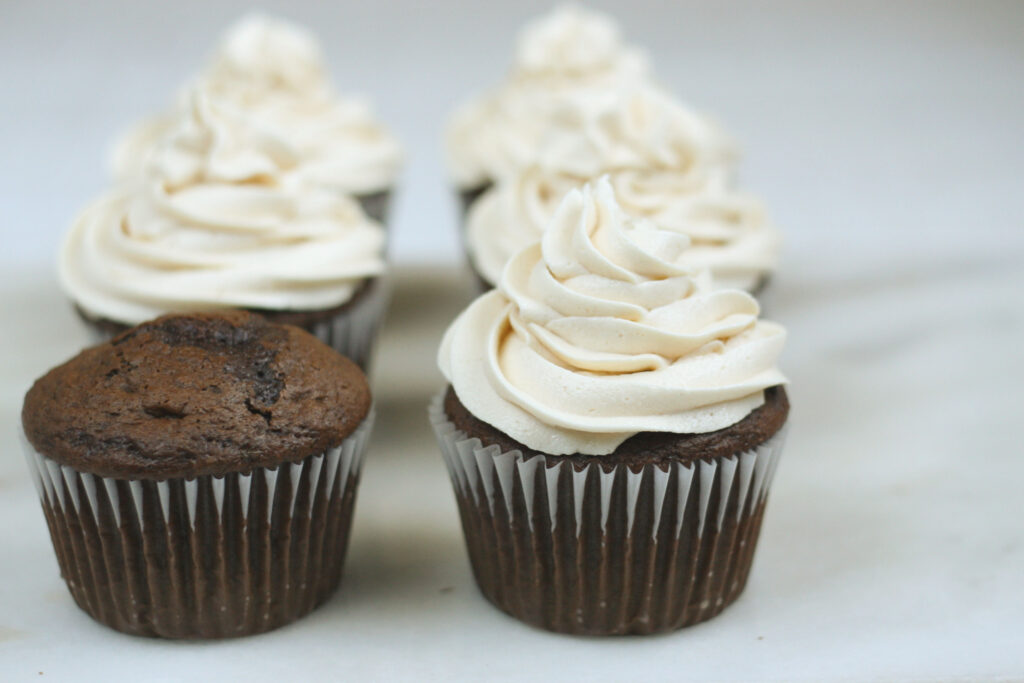 Chocolate cupcakes being piped with peanut butter cream cheese frosting