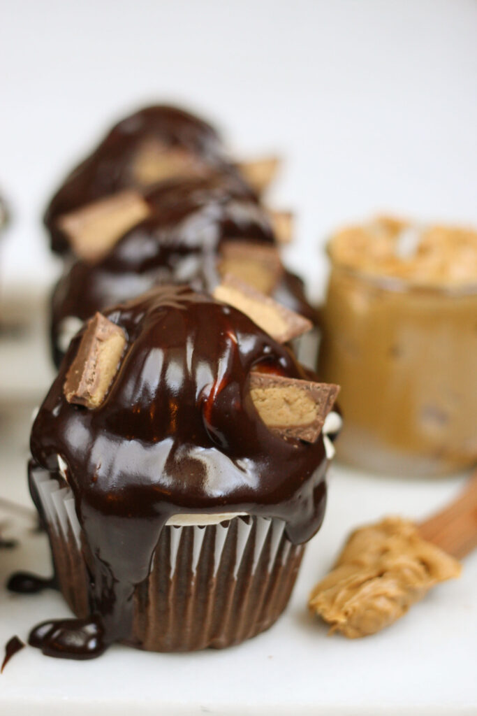 close up of chocolate cupcake with peanut butter frosting, drizzled with chocolate ganache, and pieces of peanut butter cups in frosting