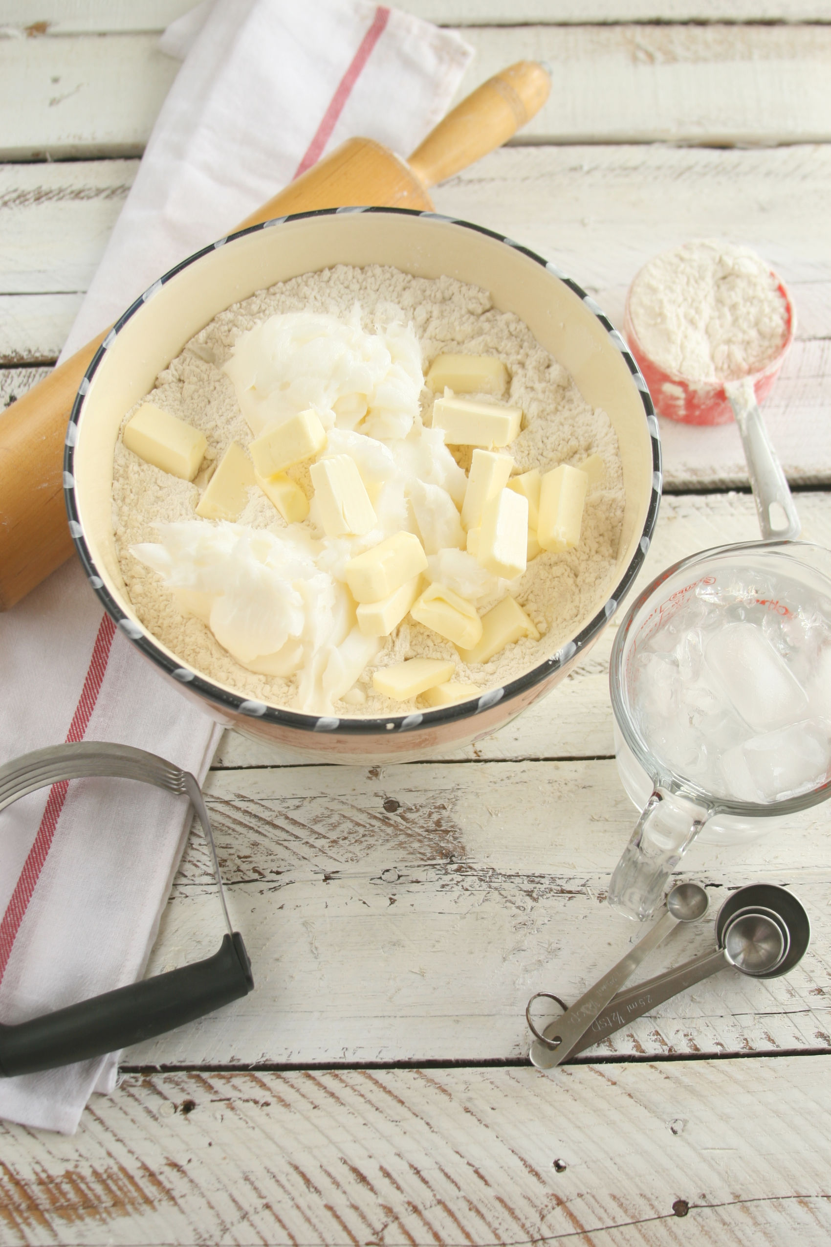 Ceramic bowl with flour, lard, and butter being cut in with a pastry cutter