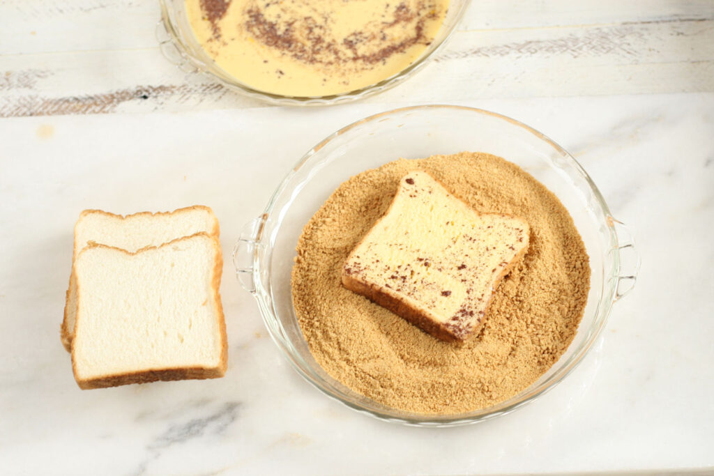 Graham cracker crumbs in a clear glass pie plate and rolling French toast pieces in it