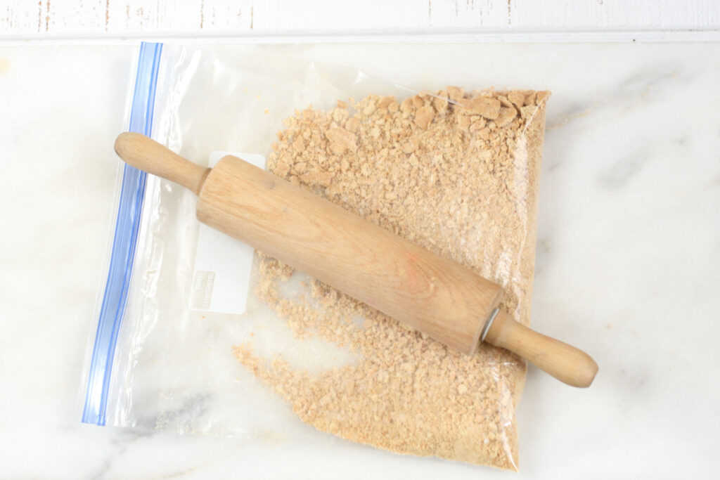 Crushing Graham crackers in a large Ziploc bag with a small wooden rolling pin