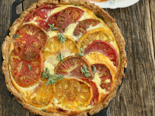 homemade quiche with heirloom tomatoes and spinach in a large cast iron skillet with a small glass plate of sliced tomoatoes near it