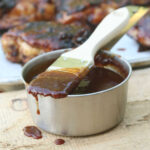 Pastry brush dripping with BBQ sauce on metal measuring cup.