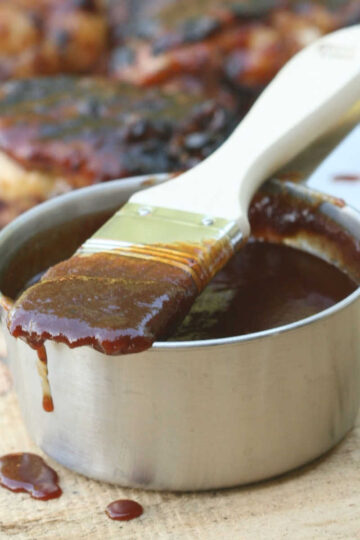 Pastry brush dripping with BBQ sauce on metal measuring cup.