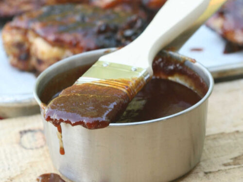 Pastry brush dripping with BBQ sauce on metal measuring cup.