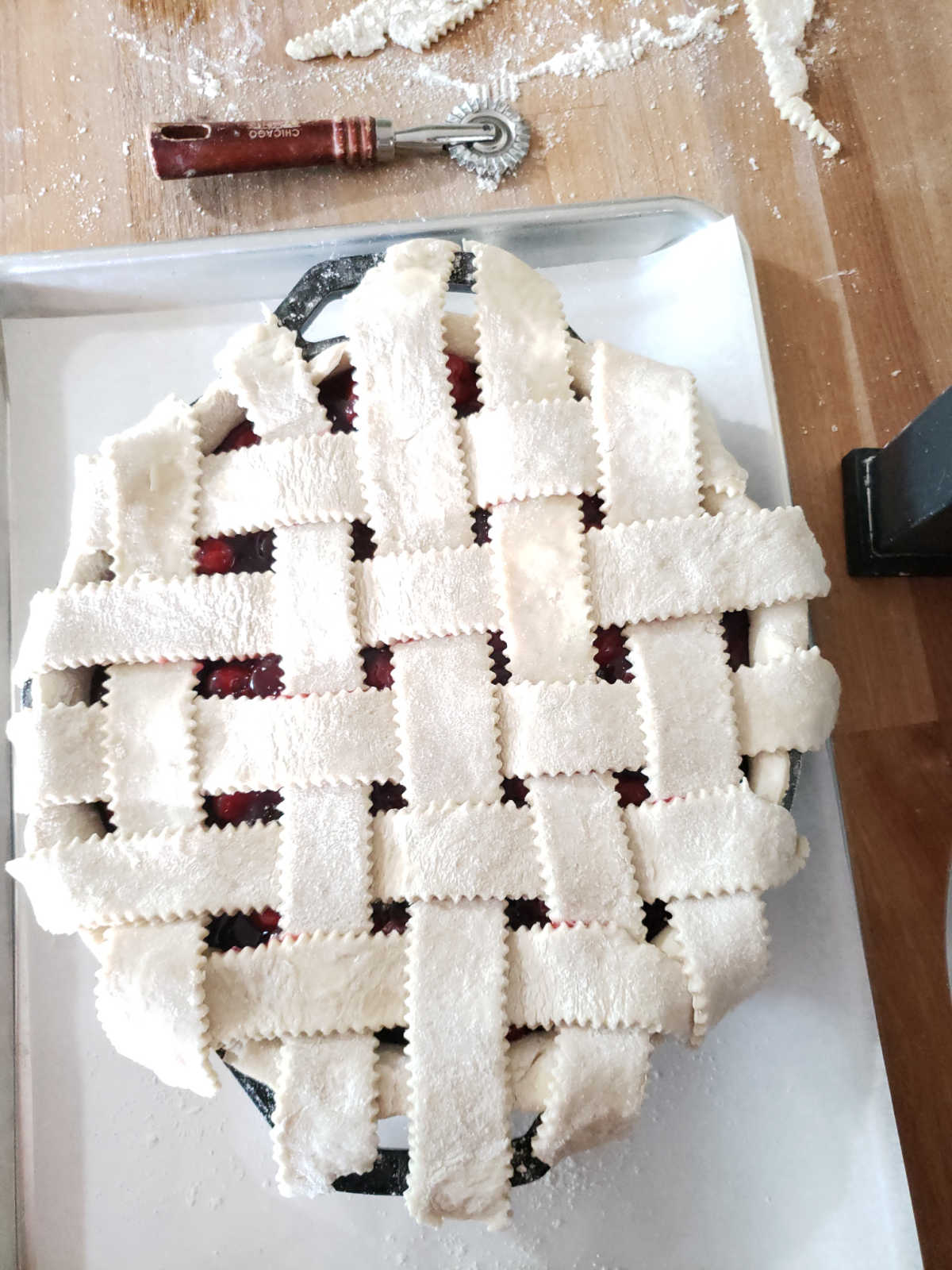 Unbaked cherry pie with lattice crust on metal baking pan on butcher block.