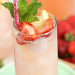 Strawberry lemonade in clear glass with ice cubes and lemon wedge.