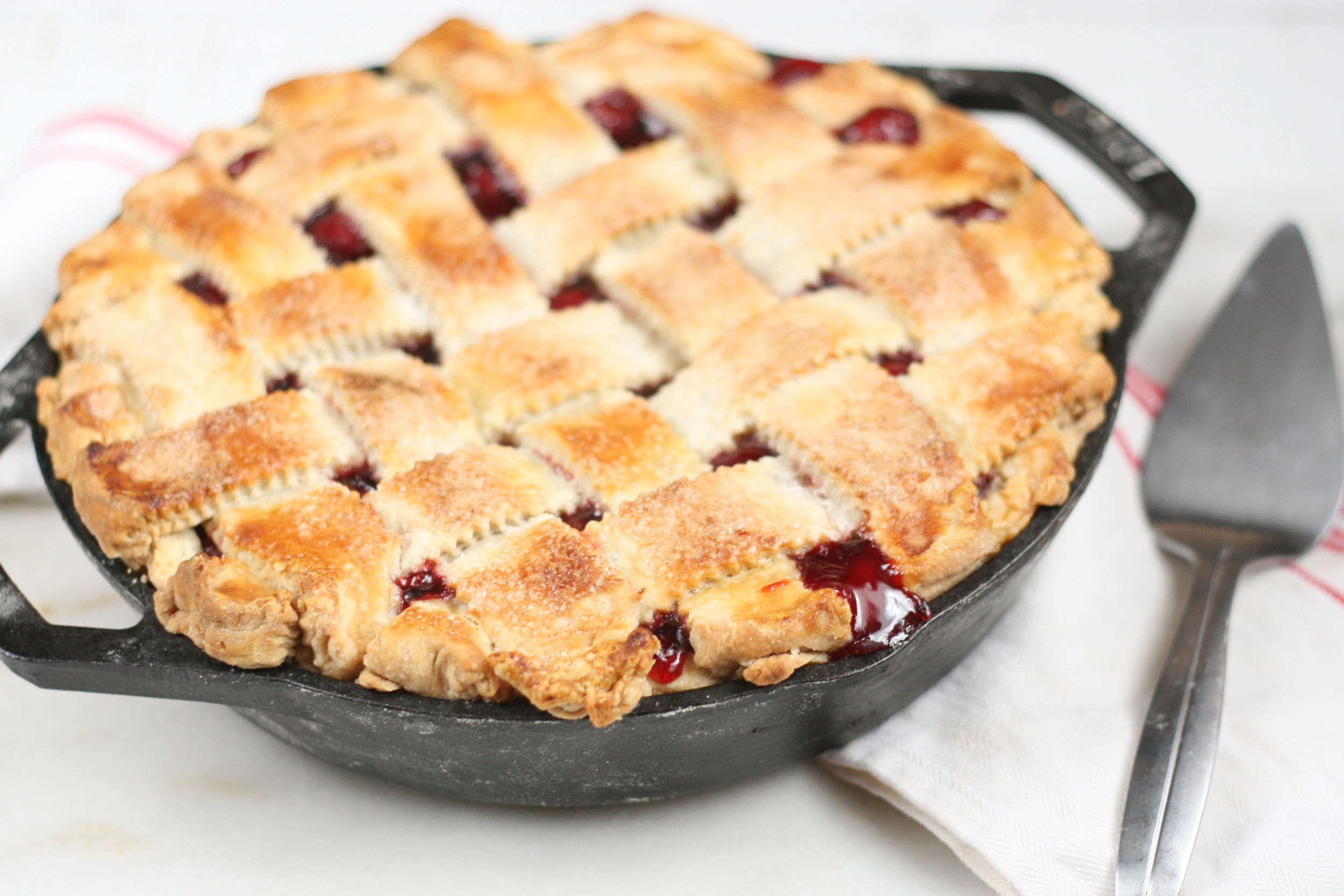 homemade cherry pie with lattice crust in a 2-handle cast iron skillet.