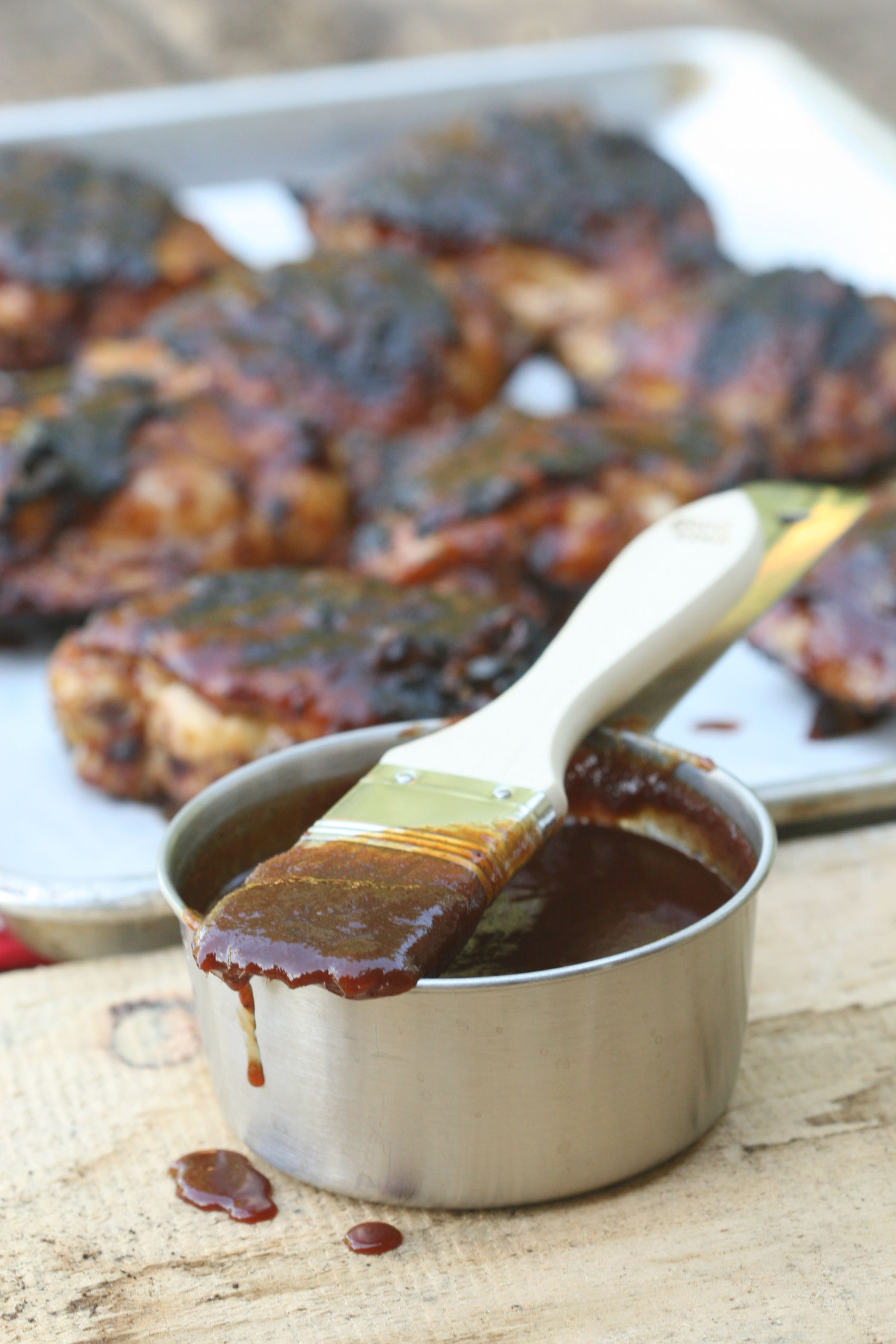 homemde barbecue sauce in metal measuring cup and wooden handle brush dripping with barbecue sauce.
