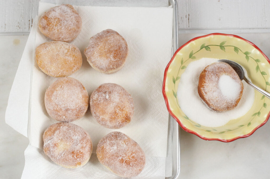 rolling freshly fried donuts in granulated sugar in a bowl.