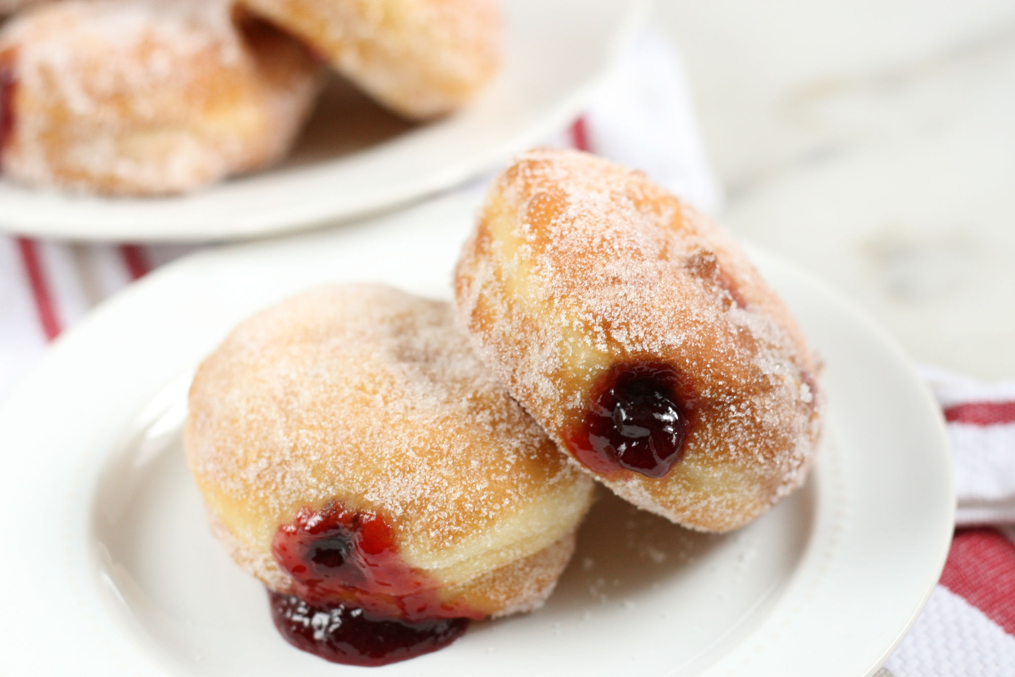 two jelly donuts dusted in sugar and filled with raspberry jam sitting on a white plate