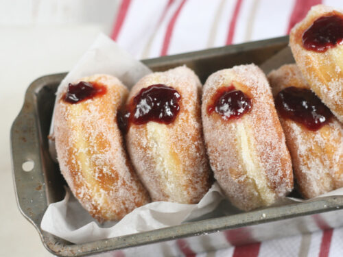 jelly donuts lined up against each other in a metal loaf pan lined with parchment paper